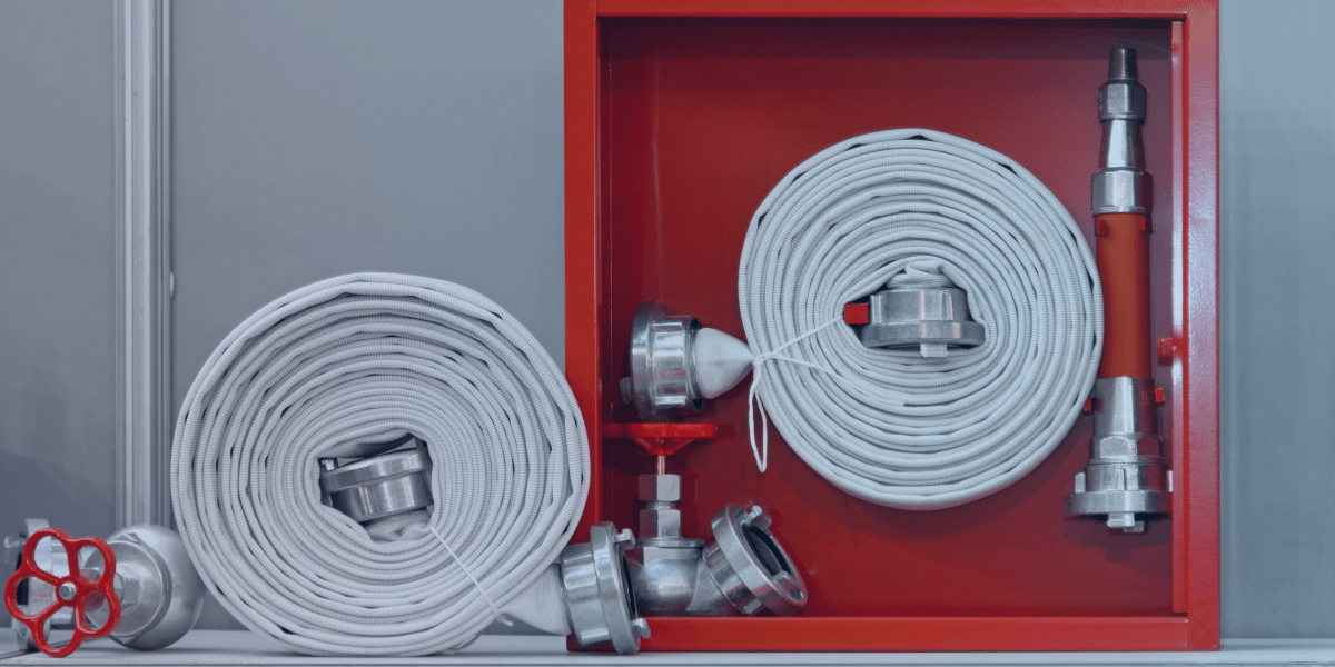 duas mangueiras de incêndio enroladas ao lado da outra. a mangueira da direita está em uma caixa vermelha de incêndio. a mangueira da esquerda está fora dela.